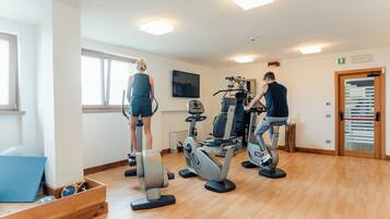 Un gimnasio con equipamiento de ejercicio, televisión y suelo de madera.