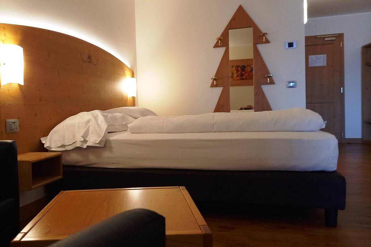 A hotel room with a bed, a wooden headboard with a light, a mirror, a wooden table, and a black chair.