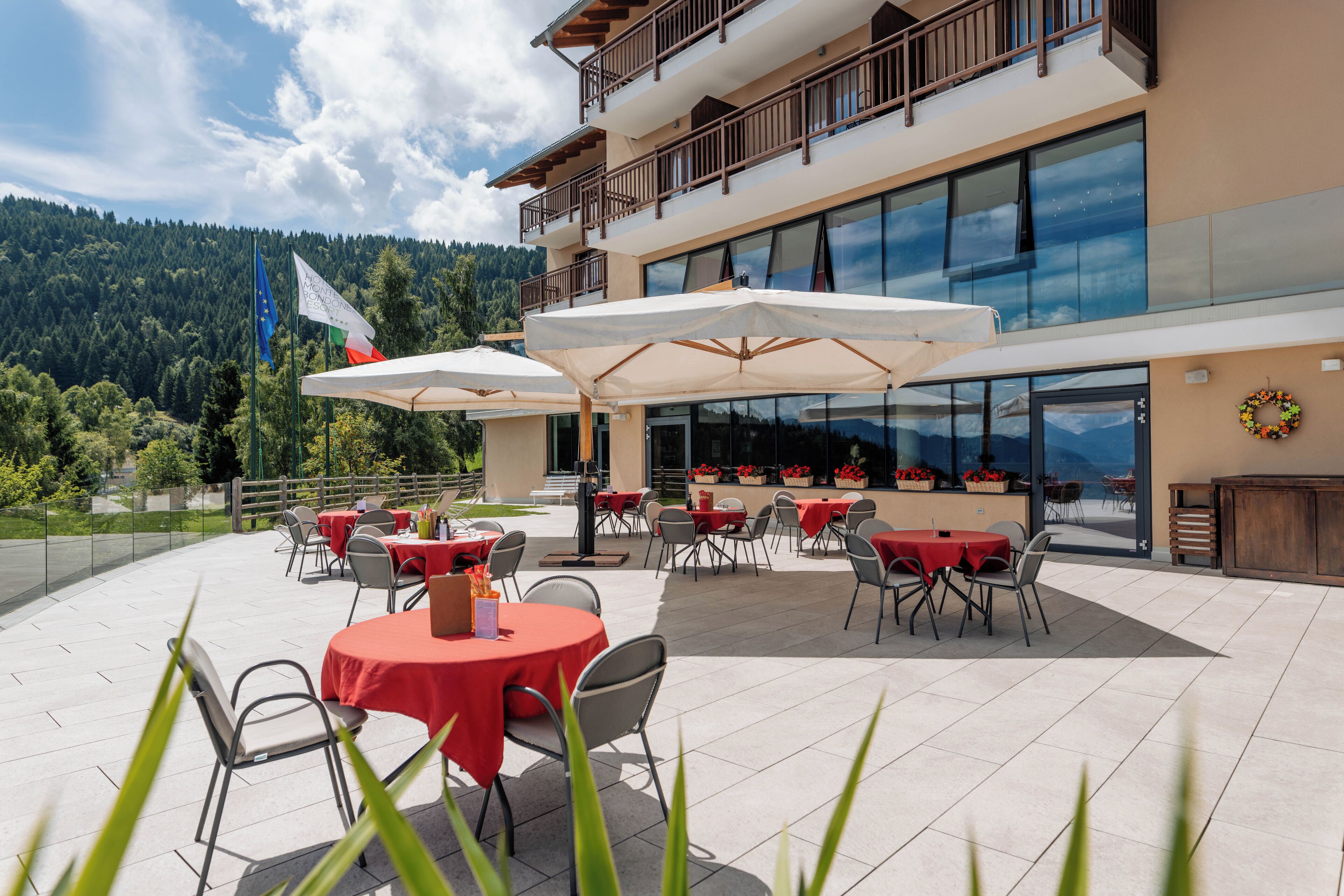 An outdoor patio with round tables and chairs, a flag, and a view of a forested mountain range.