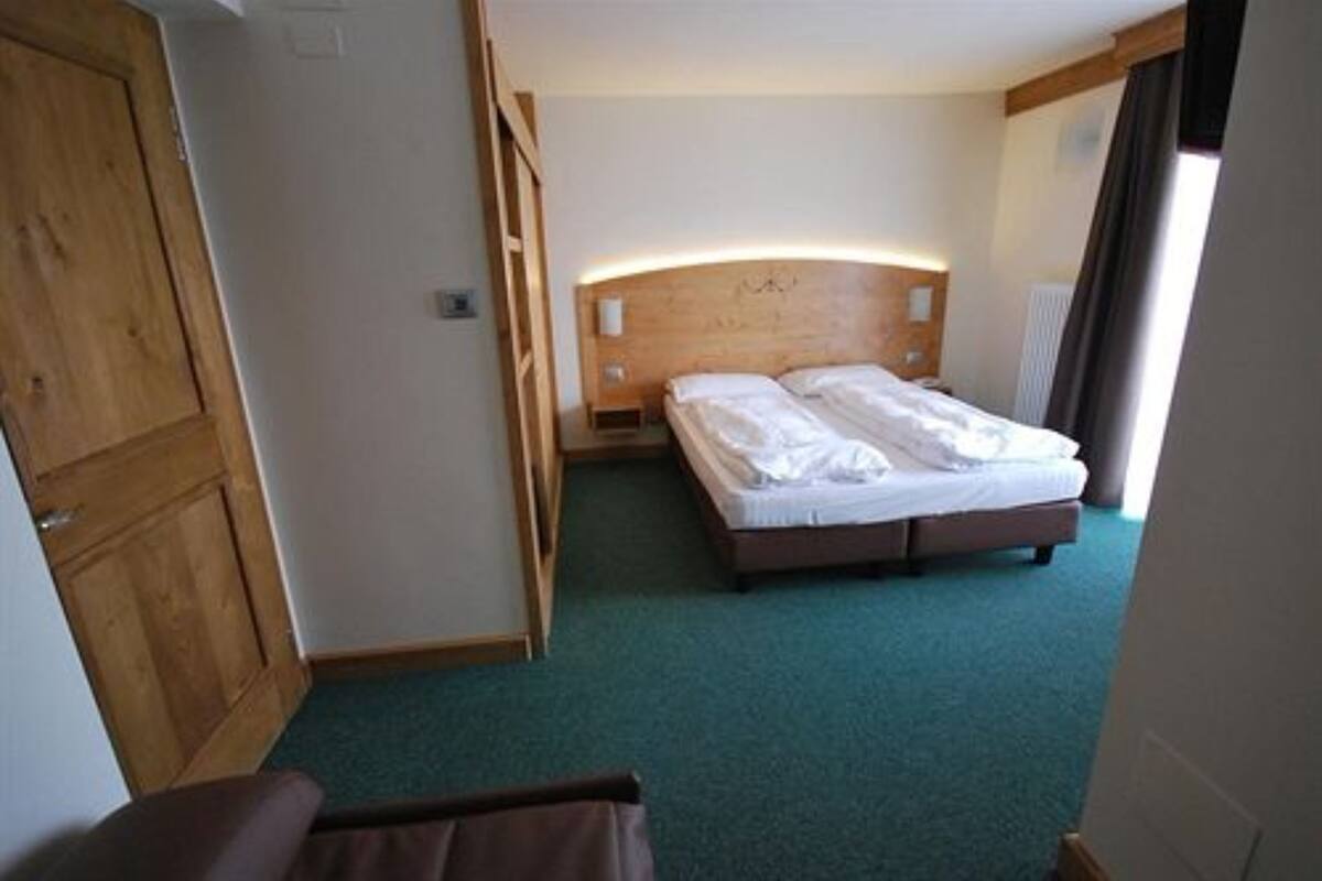 A bedroom with a wooden headboard, a bed with white linens, and a green carpet.
