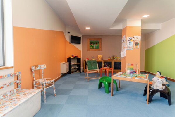 Un cuarto de juegos infantil con alfombra azul, paredes anaranjadas, una mesa de madera con juguetes y un taburete verde.