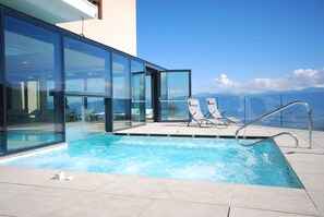 Una piscina infinita moderna con agua azul cristalina, rodeada por paredes de vidrio y una barandilla metálica.