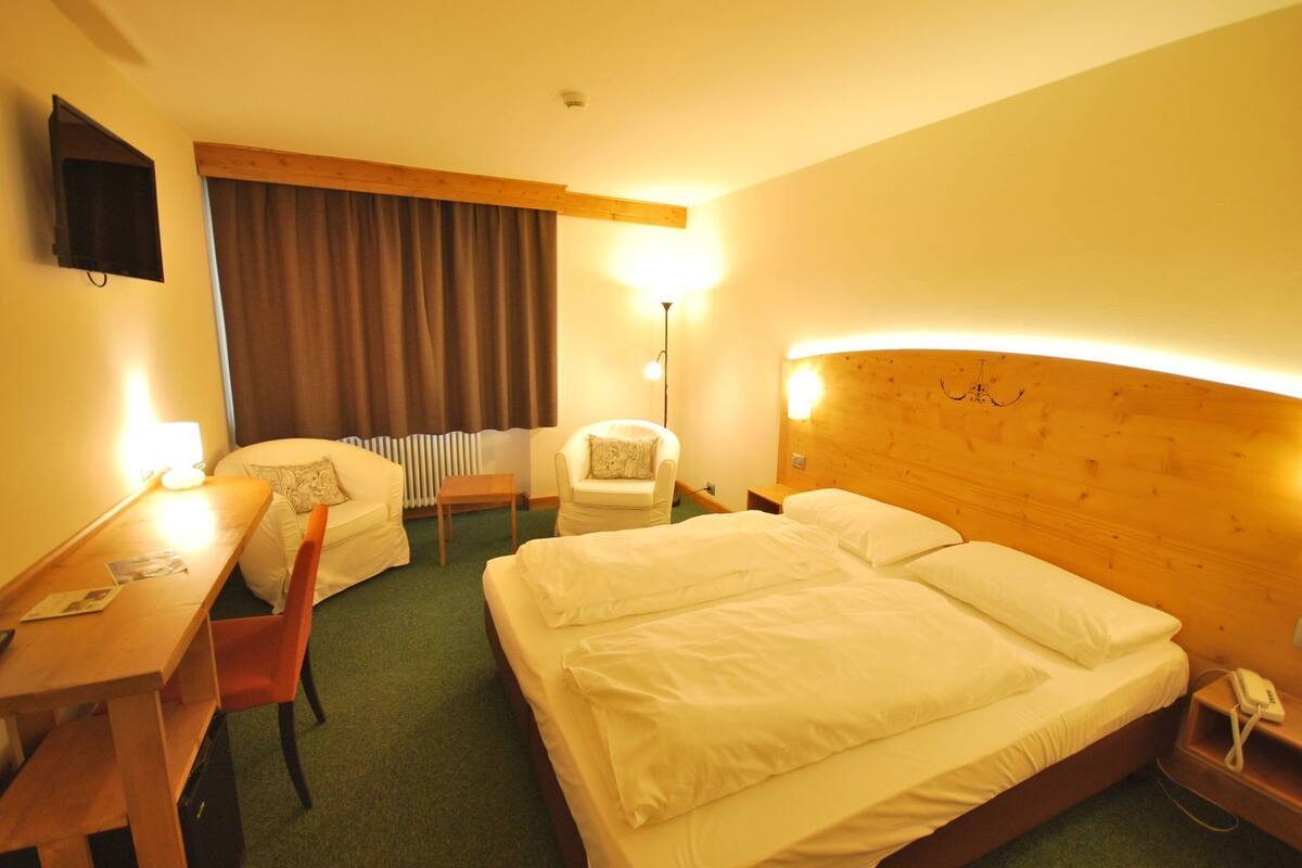 A hotel room with a bed, a desk, a chair, a lamp, and a television.