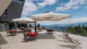 Terraza exterior con mesas y sillas, sombrillas y vistas a las montañas.