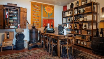 Ein Zimmer mit einem Holztisch, Stühlen, einem großen Teppich, Regalen mit Flaschen und einem dekorativen Wandelement.