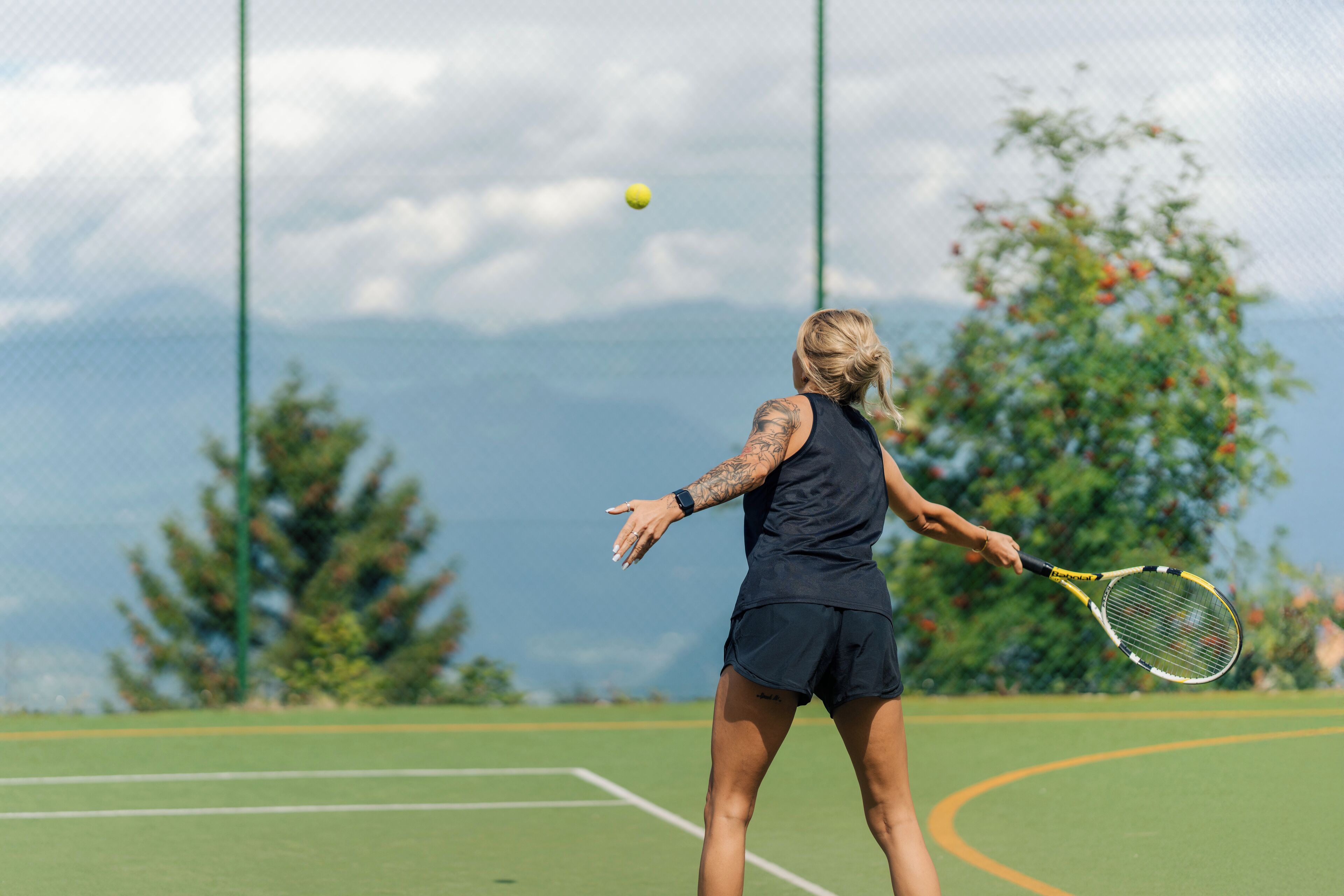 A tennis player on a court with a net, trees, and mountains in the background.