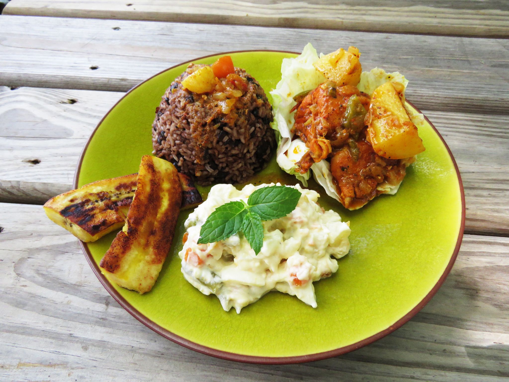En tallrik med olika rätter, bland annat en stor portion ris, en skål med curry, grillade grönsaker och en klick potatissallad.