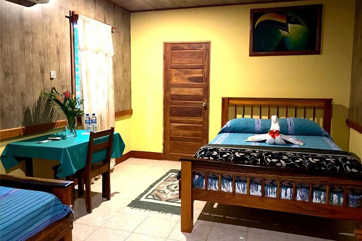 A room with a bed, a desk with a chair, a window with curtains, a wooden door, and a painting on the wall.