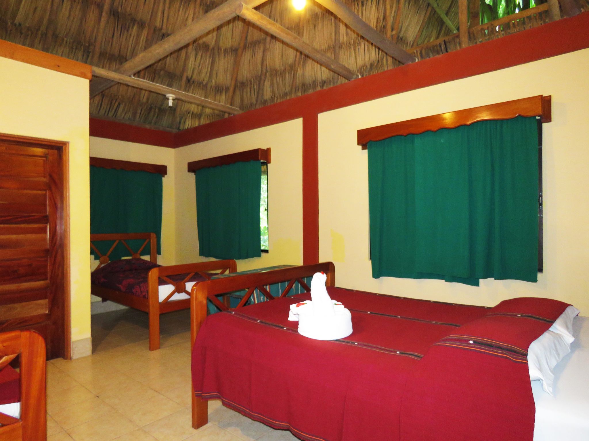 A room with a bed, a wooden bench, and a table with a red tablecloth.