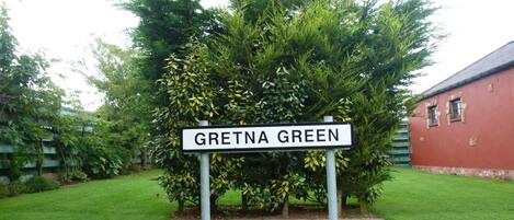 Un panneau de signalisation indiquant « Gretna Green », placé dans un jardin, avec un bâtiment rouge en arrière-plan.