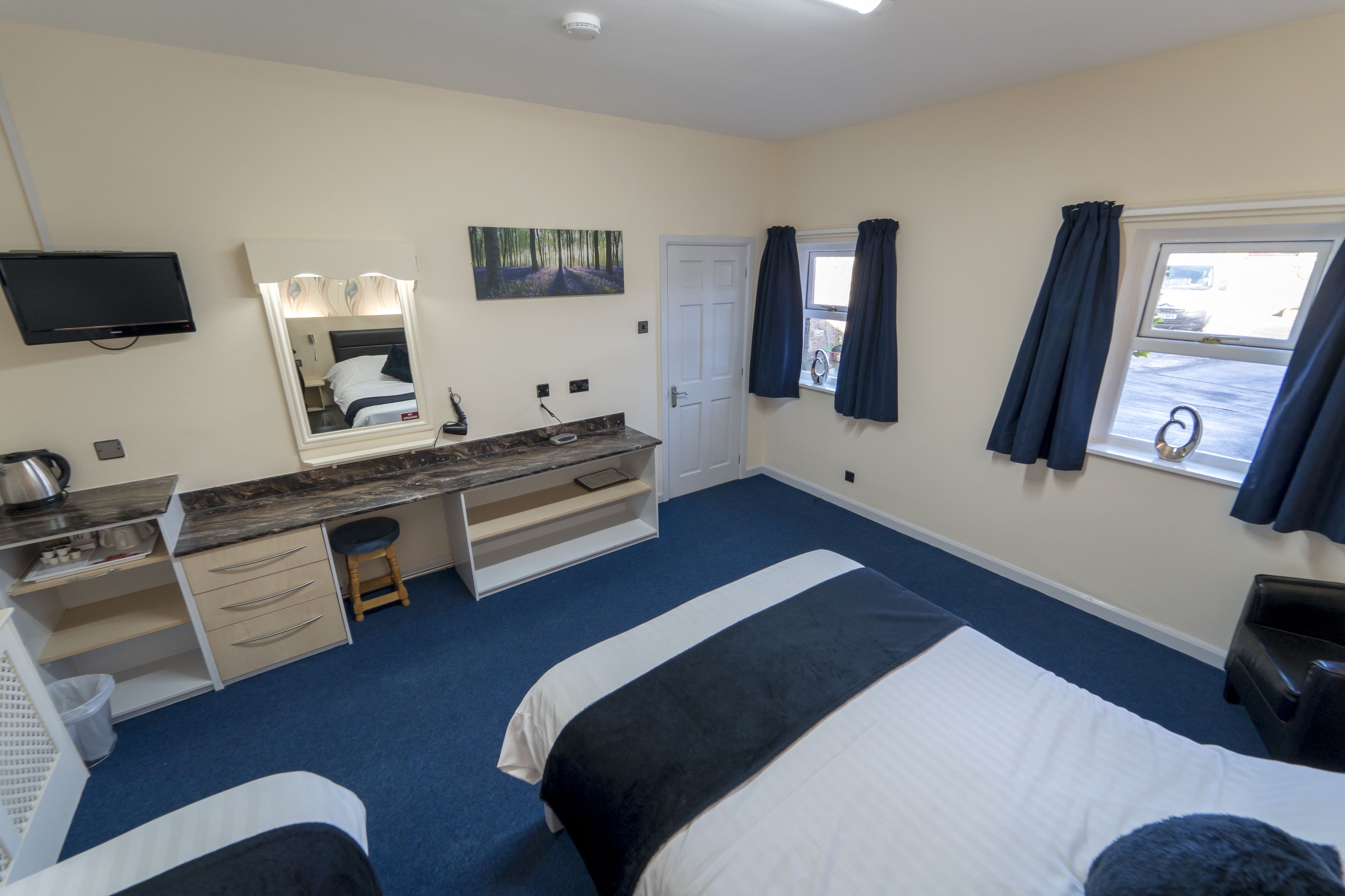 A hotel room with a bed, a desk with a chair, a mirror, a television, and a window with curtains.