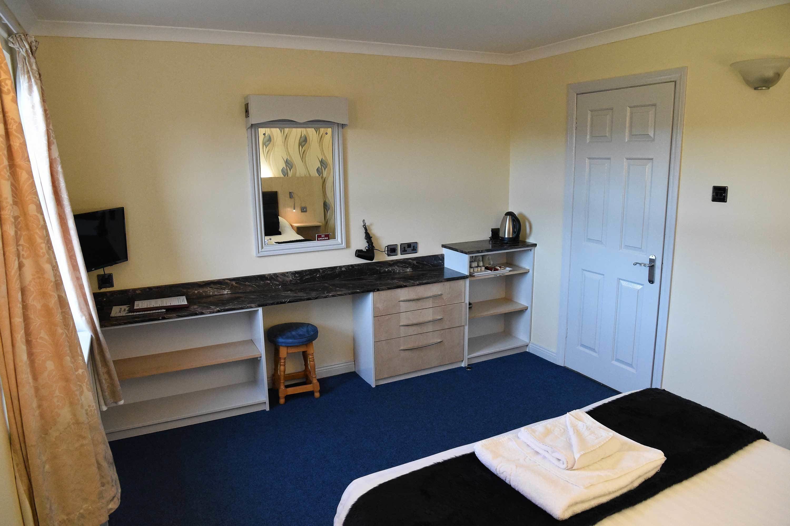 Une chambre à coucher de taille réduite, comprenant un lit, un bureau avec une chaise, un miroir, un téléviseur et une porte.