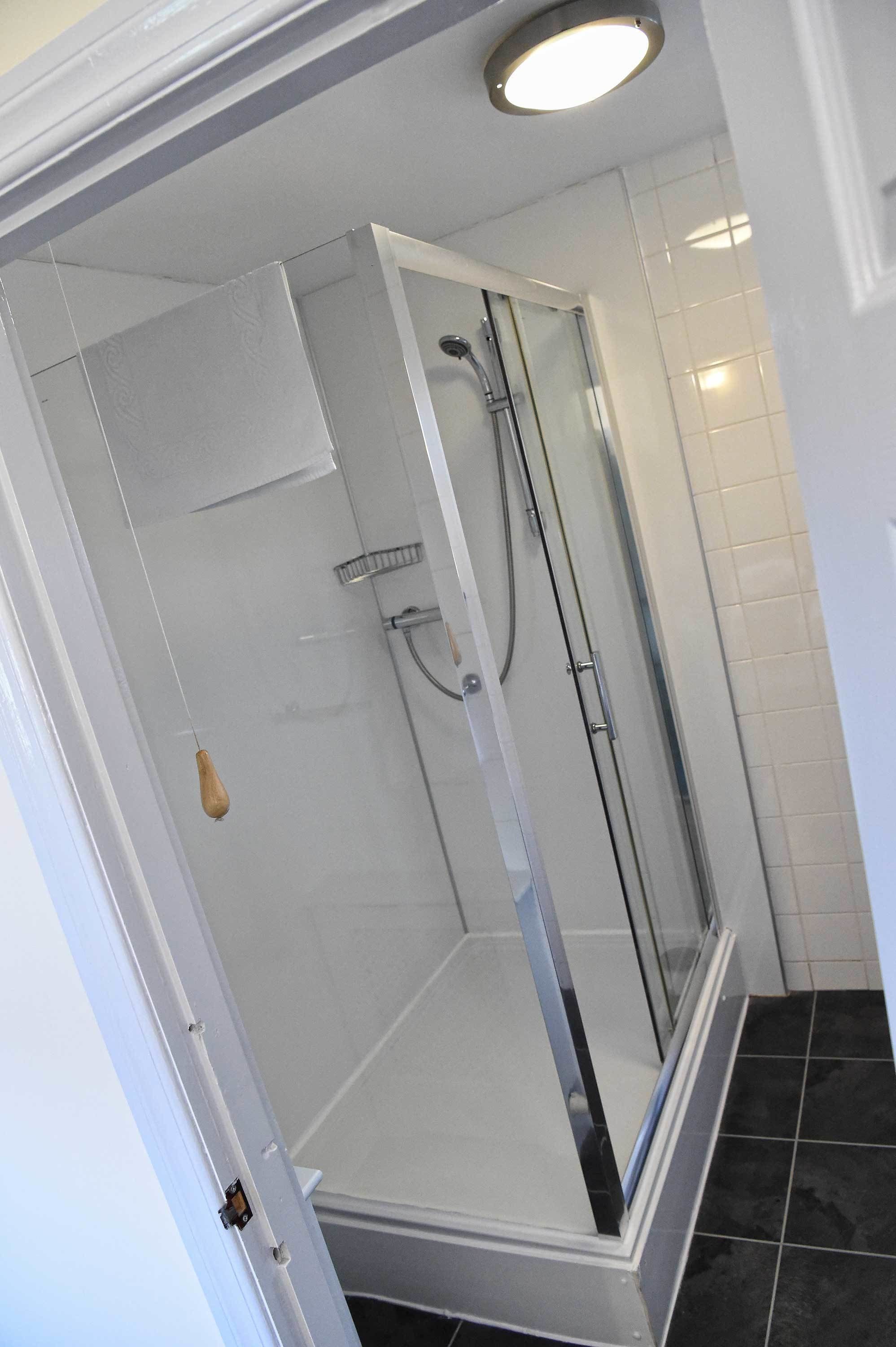 A modern shower enclosure with a glass door, a handheld showerhead, and a wall-mounted faucet.