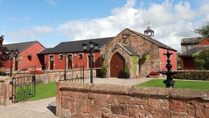 A historic building with a stone facade, red brick walls, and a traditional arched entrance. - The Mill Forge (Lockerbie)