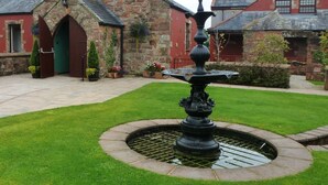 A courtyard with a fountain, stone buildings, and a well-maintained lawn. - The Mill Forge (Lockerbie)