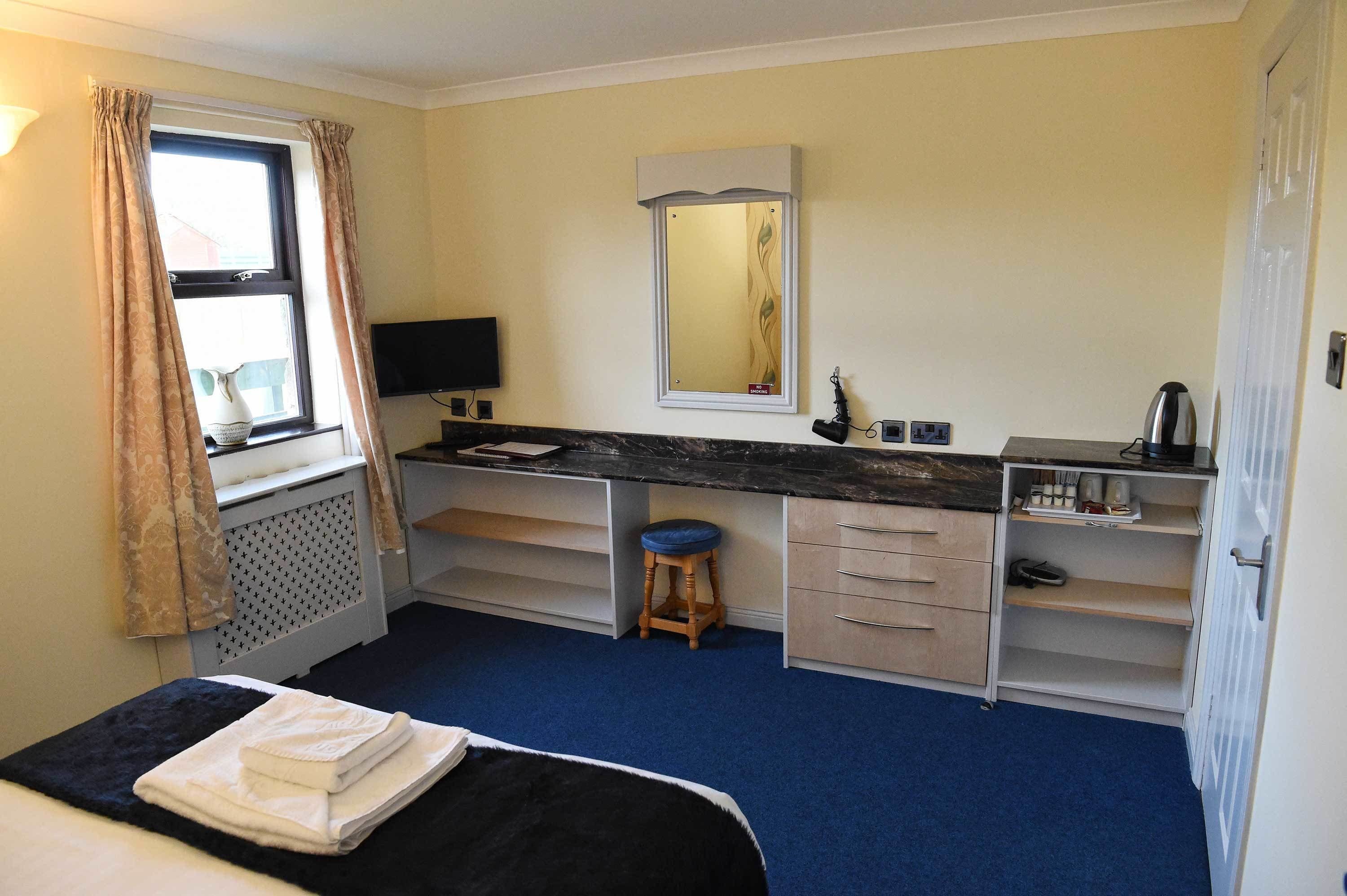 A hotel room with a bed, a desk with a computer, a mirror, and a window with curtains.