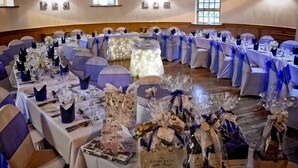 A banquet hall with round tables set for a formal event, featuring blue and white tablecloths and matching chair covers. - The Mill Forge (Lockerbie)