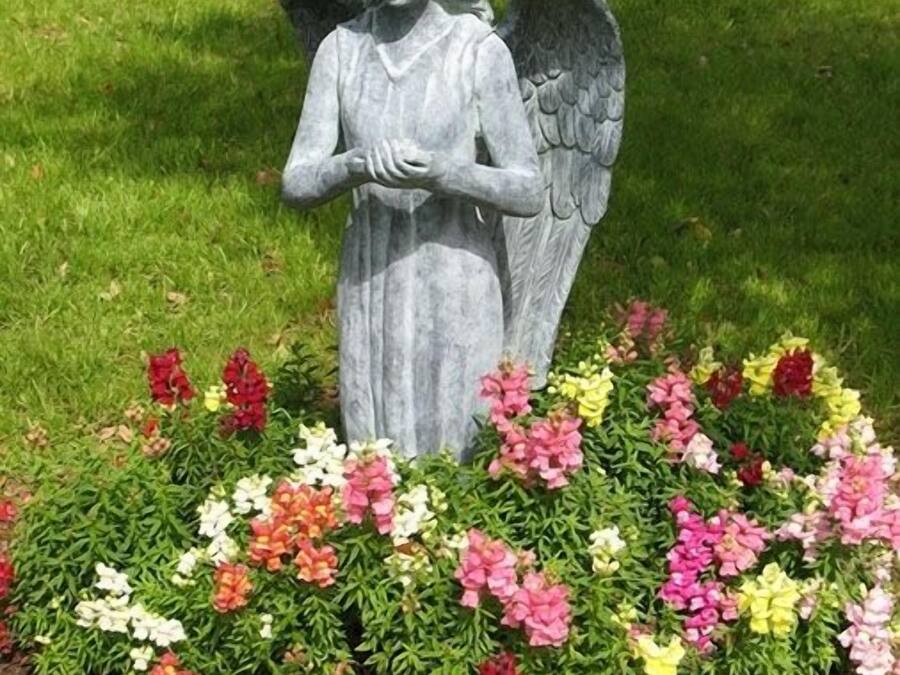 A garden statue of an angel surrounded by a variety of colorful flowers.