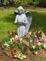 A garden statue of an angel surrounded by a variety of colorful flowers.