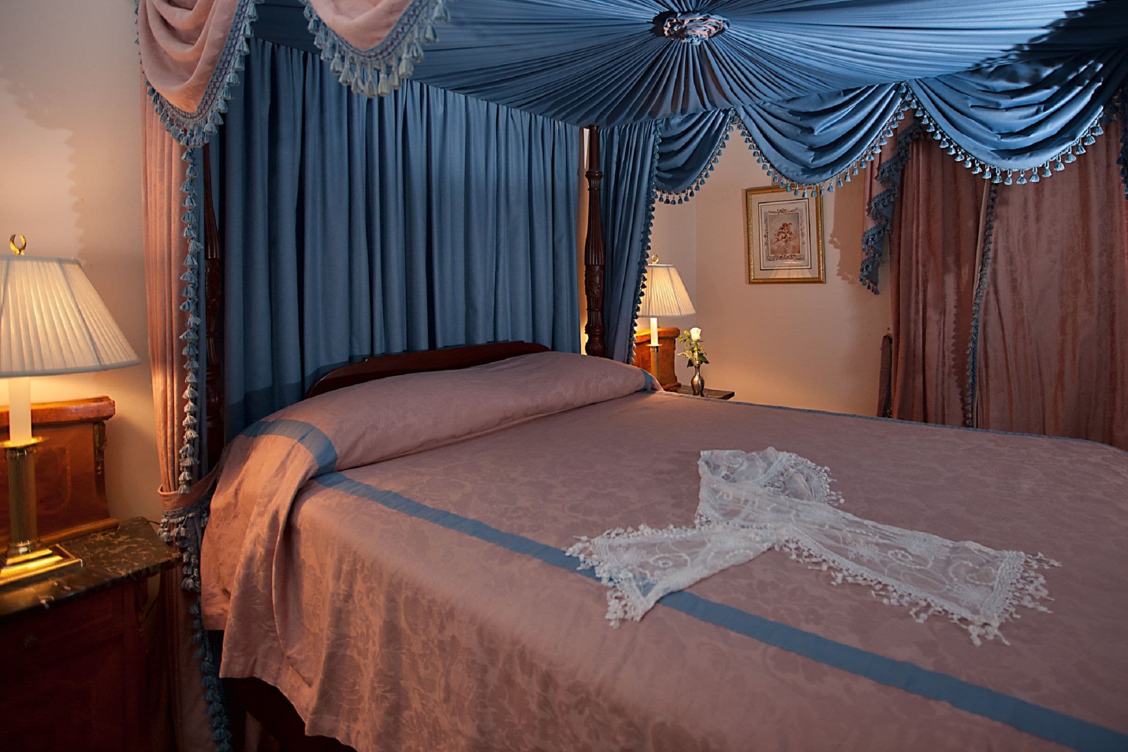 A bedroom with a large bed, a nightstand with a lamp, and a canopy bed with draped curtains.