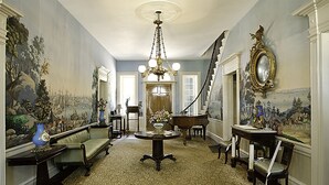 Una sala imponente con candelabro, un piano, un sofá y una mesa con un jarrón de flores.