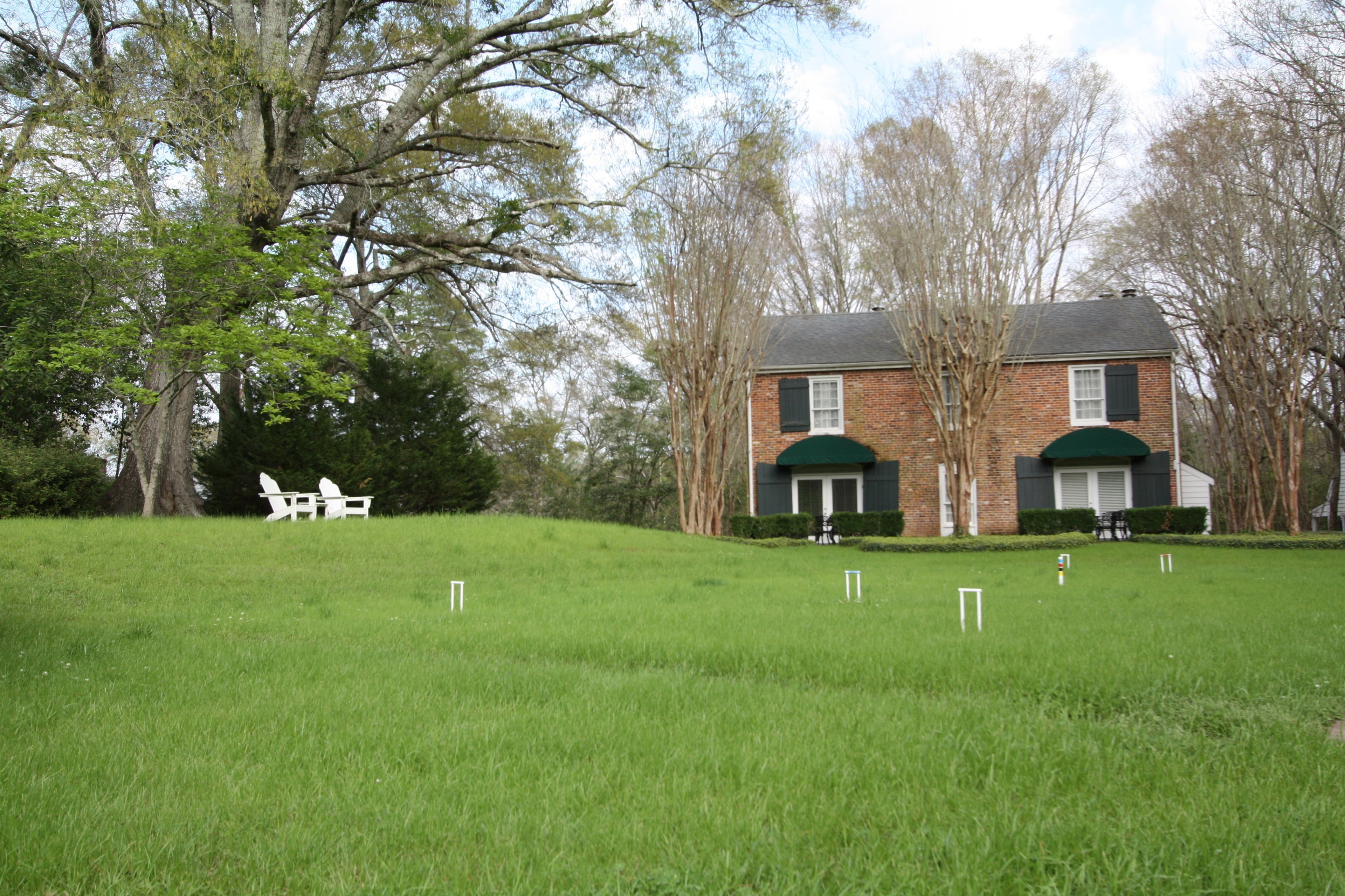 A brick building with a green roof, surrounded by a grassy field and trees.