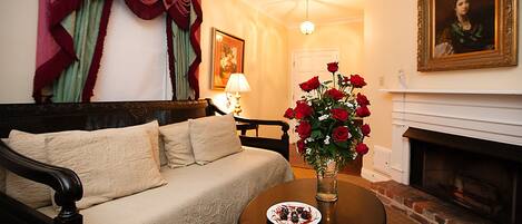 Ein gemütliches Wohnzimmer mit einer Couch, einem Tisch mit einer Vase roter Rosen, einem Kamin und einem Gemälde an der Wand.