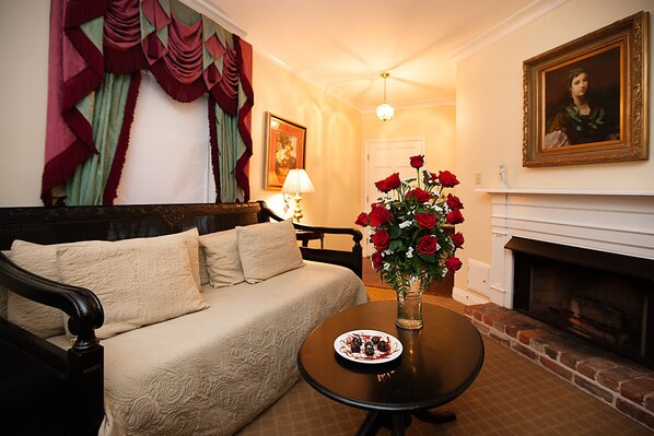 A cozy living room with a sofa, a table with a vase of red roses, a fireplace, and a painting on the wall.