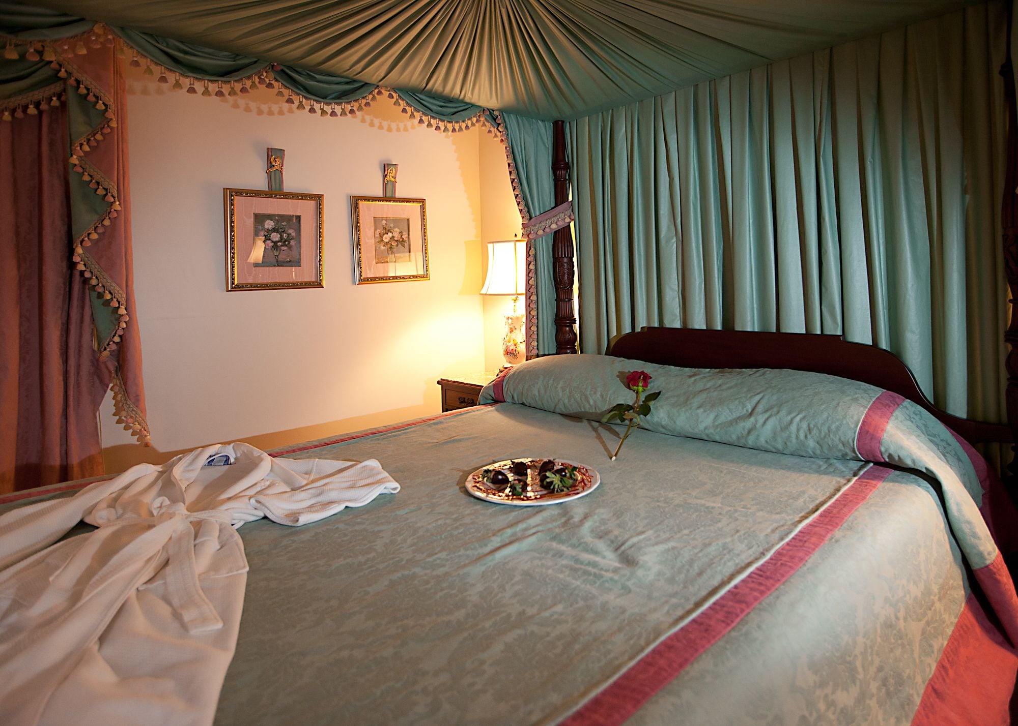 A neatly made bed with a floral pillow, a plate of food, and a rose on the bed.
