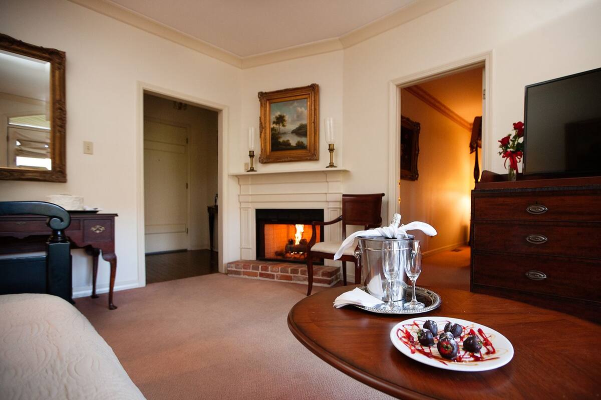 A hotel room with a fireplace, a dining table with a plate of food, a TV, and a bed.