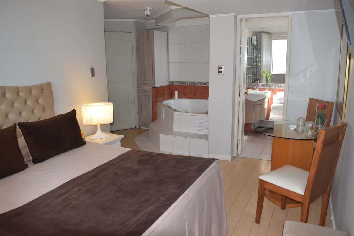 A hotel room with a bed, a desk, a chair, a bathroom with a bathtub, and a mirror.