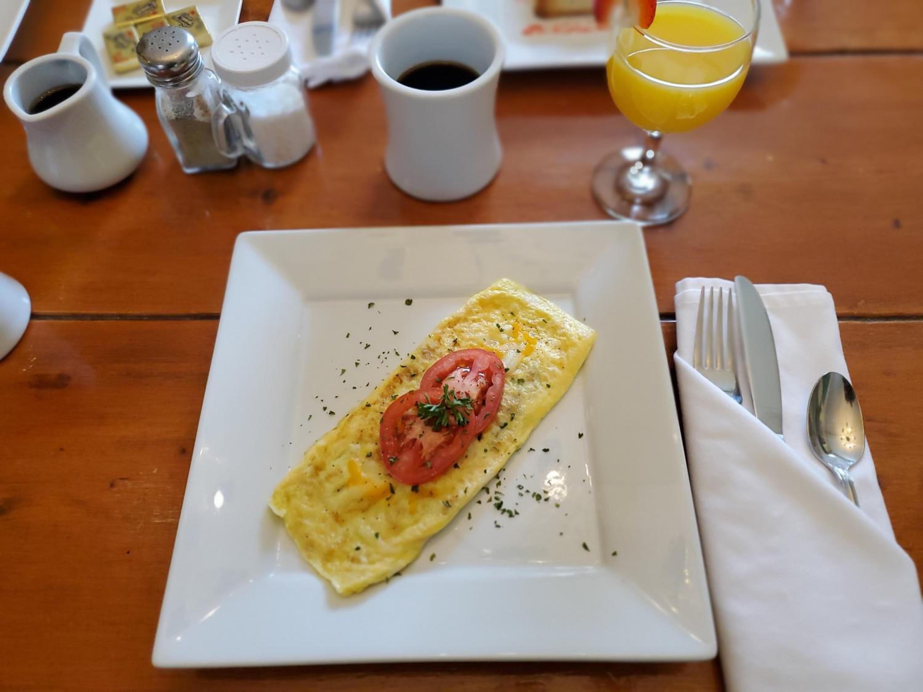 A plate with an omelette, a glass of orange juice, and salt and pepper shakers on a wooden table.
