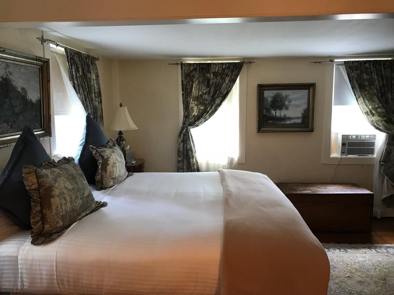 A hotel room with a large bed, two nightstands, a lamp, a painting, and a window with curtains.