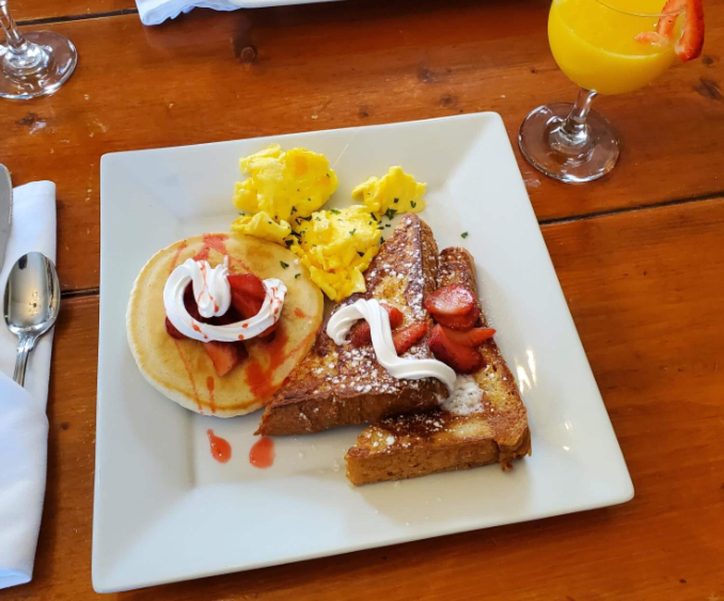 A breakfast plate with pancakes, scrambled eggs, toast, and strawberries.