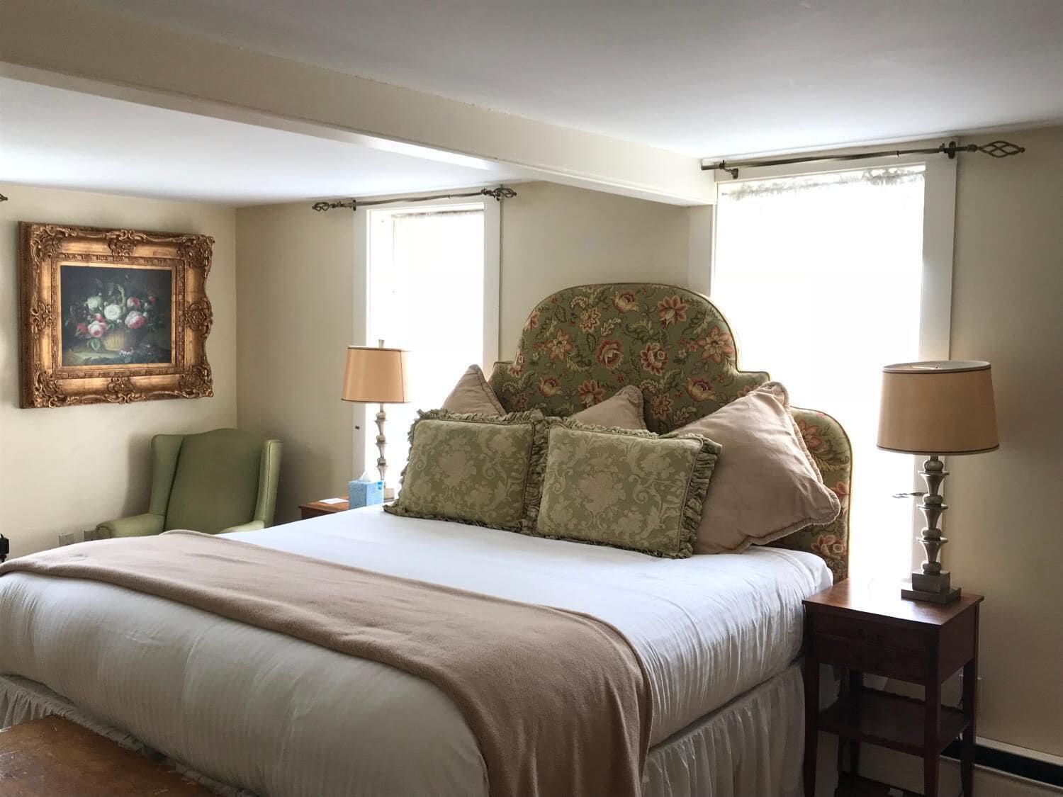 A neatly arranged bedroom with a large bed, two bedside tables with lamps, a chair, and a floral-patterned headboard.