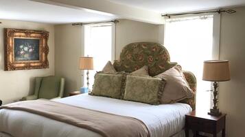 A neatly arranged bedroom with a large bed, two bedside tables with lamps, a chair, and a floral-patterned headboard.