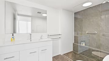 A modern bathroom with a white vanity, a large mirror, a glass shower enclosure, and a toilet.