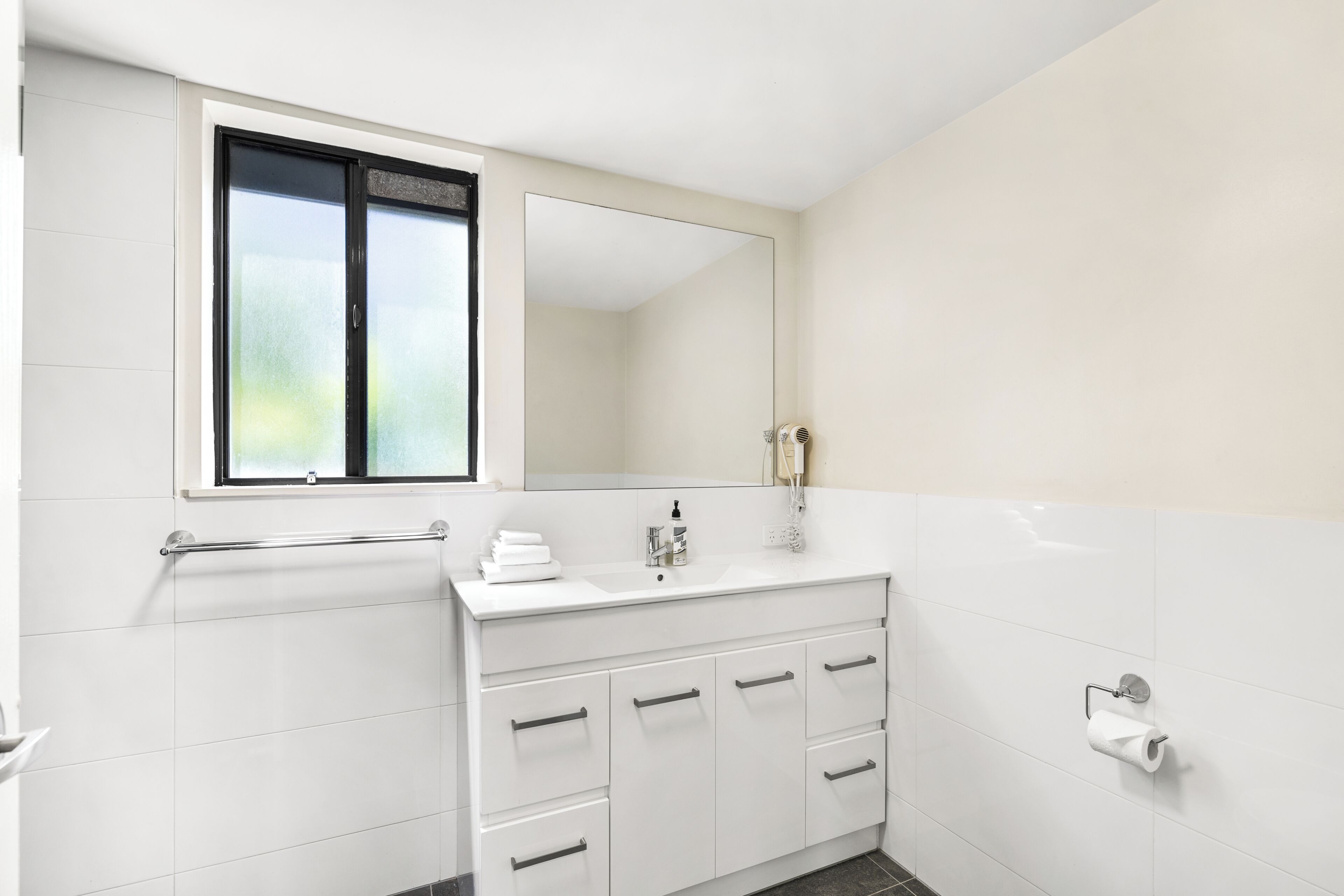 A modern bathroom with a white vanity, a mirror, a window, and a towel rack.