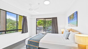A hotel room with a large bed, a ceiling fan, a view of the outdoors, and a painting on the wall. - Belaire Place Motel Apartments (Caloundra)