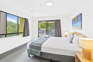 A hotel room with a large bed, a ceiling fan, a view of the outdoors, and a painting on the wall. - Belaire Place Motel Apartments (Caloundra)