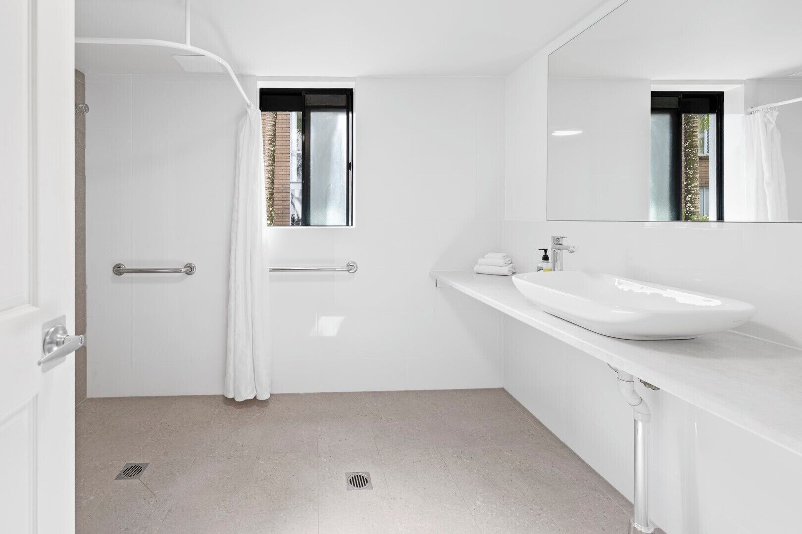 Un baño moderno con un lavamanos blanco, un espejo y una zona de ducha.