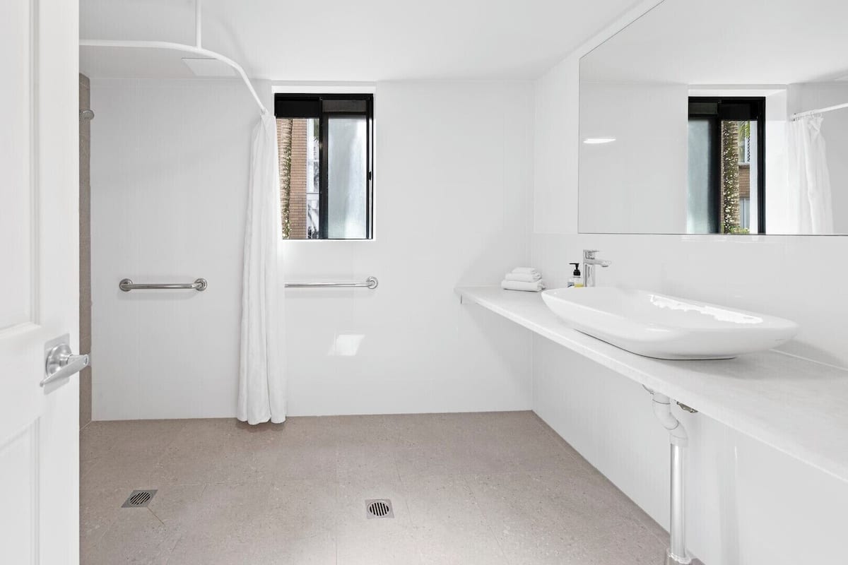 Une salle de bain moderne avec un lavabo blanc, un miroir et un espace douche.
