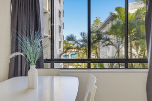 A room with a large window, a white table, and a chair. - Belaire Place Motel Apartments (Caloundra)