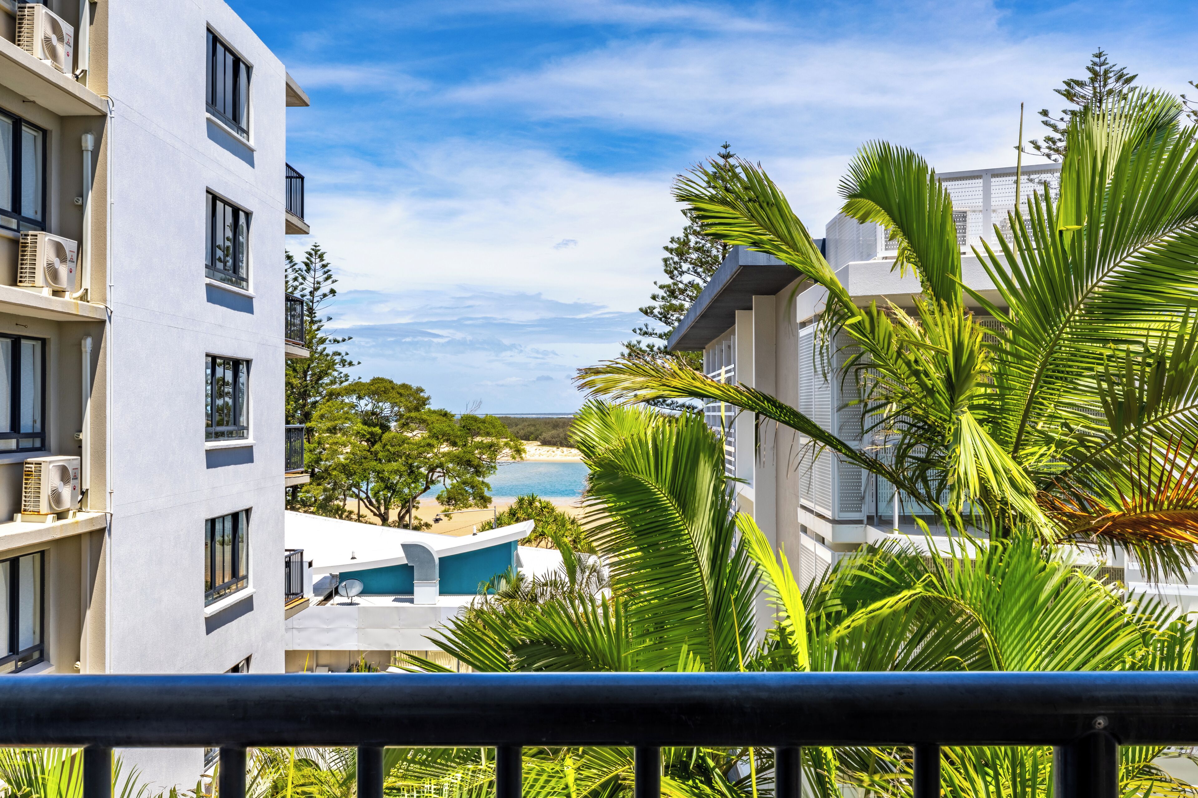 Ein modernes Hotel mit mehreren Etagen, Balkonen und einem im Hintergrund sichtbaren Poolbereich.