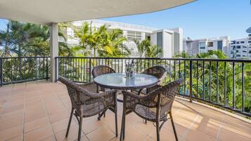 Een ronde tafel met rieten stoelen op een balkon, uitzicht op palmbomen en gebouwen.
