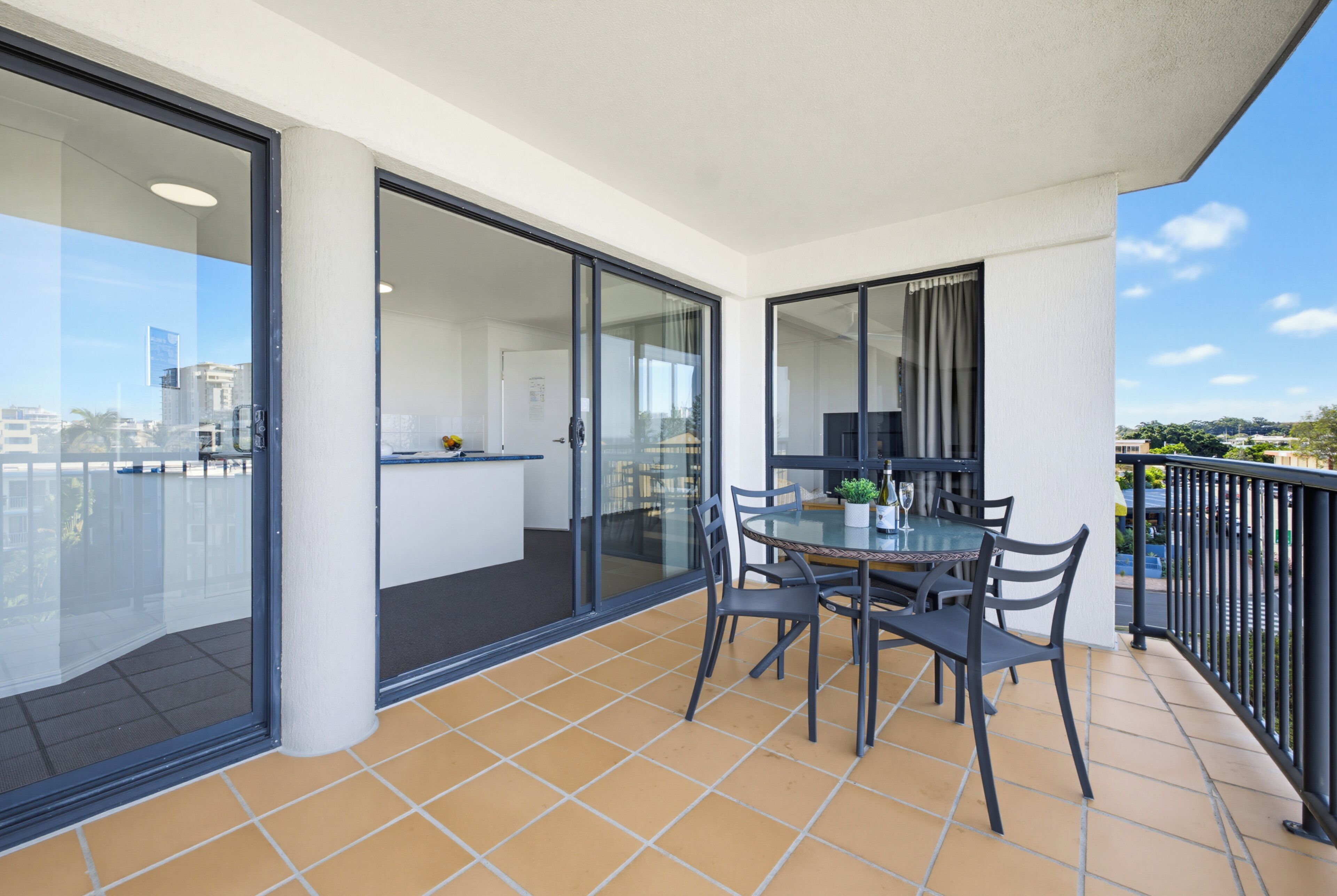 A balcony with a glass door leading to a kitchen, a dining table with chairs, and a view of the cityscape.