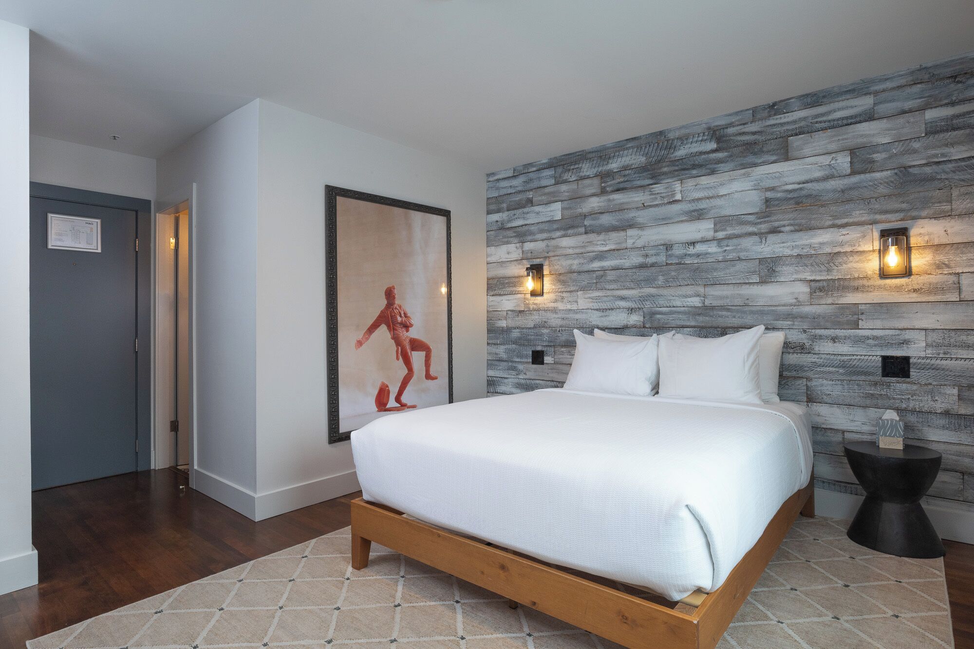 A bedroom with a wooden bed, a gray wall with a textured pattern, and two wall-mounted lights.