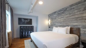 Un dormitorio con cabecera de madera, cama con ropa de cama blanca, alfombra de estampado geométrico, radiador y aplique de pared.