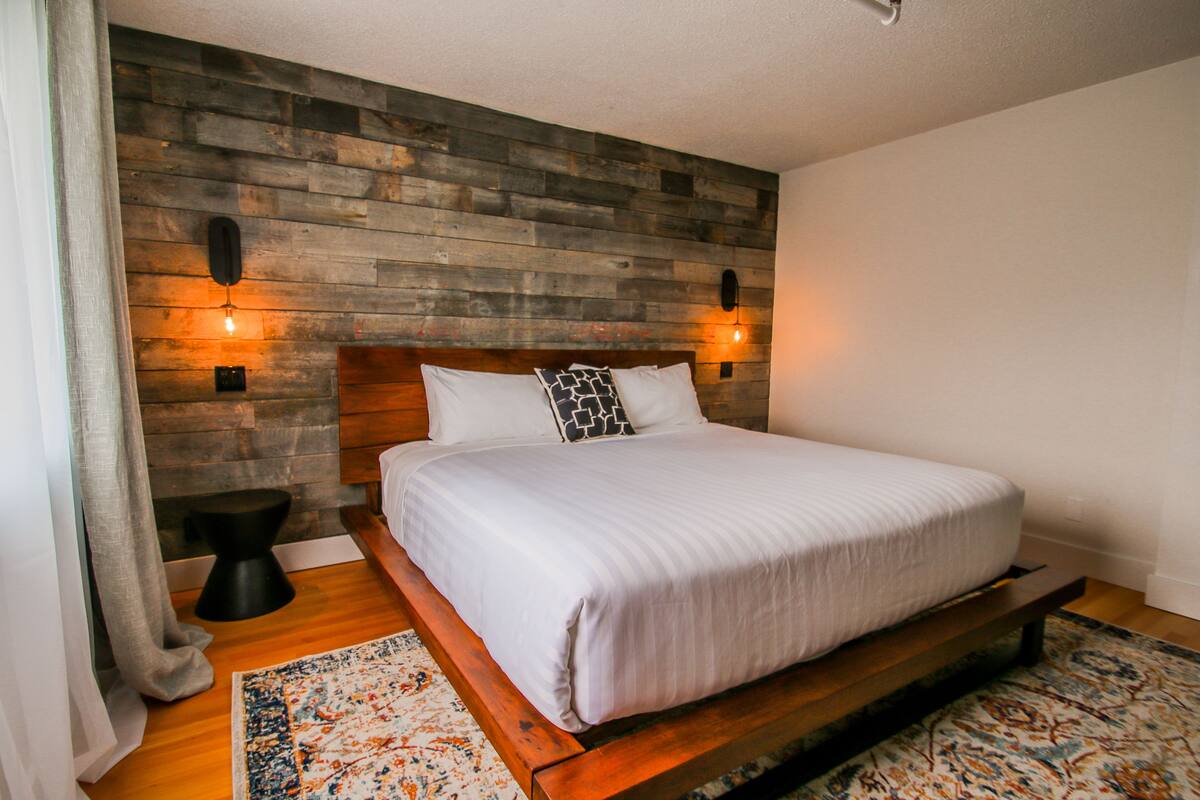 A modern bedroom with a wooden headboard, a large bed with white bedding, two bedside tables, and a patterned rug.