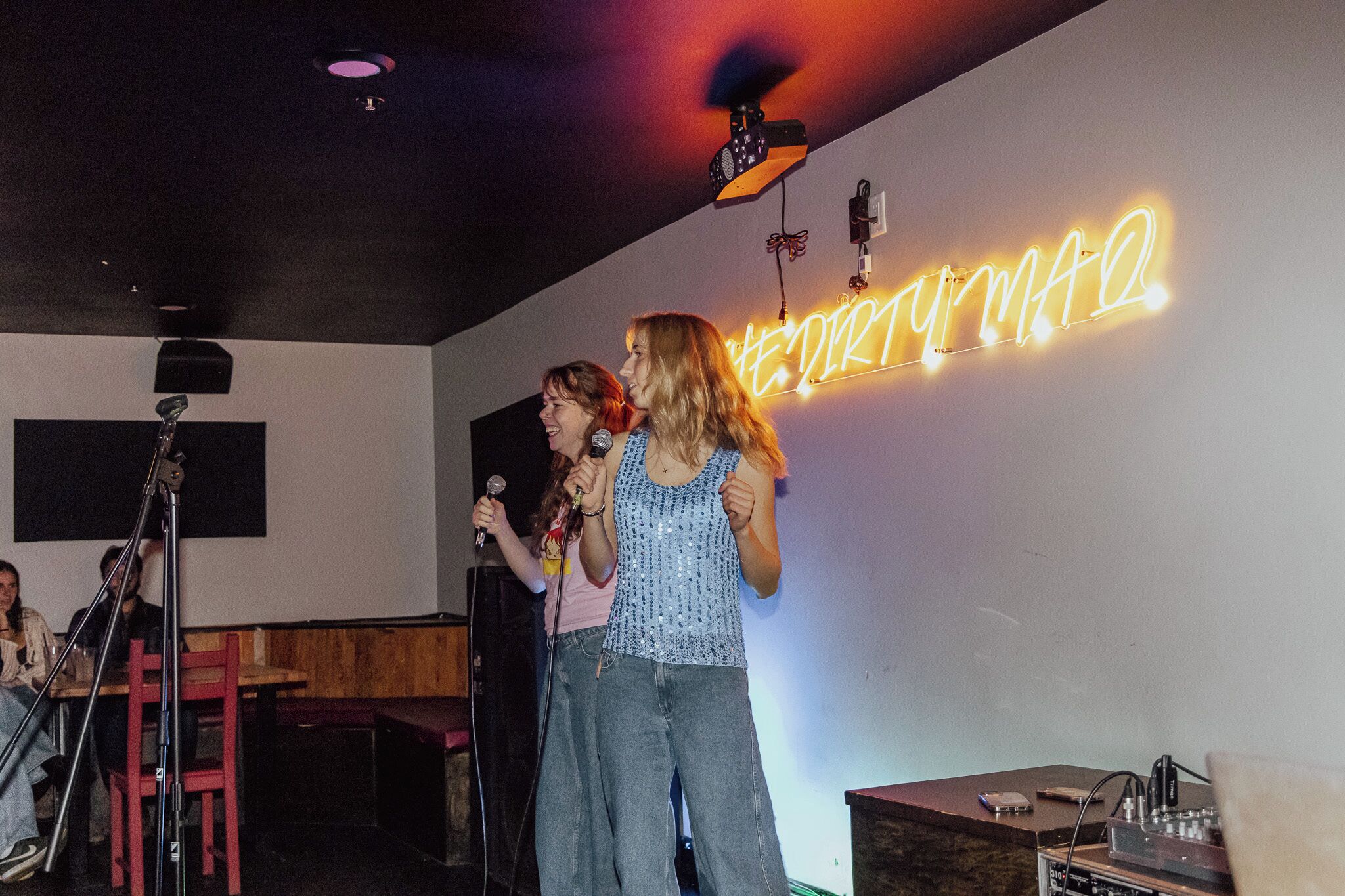 A room with a neon sign, a microphone stand, and a speaker.